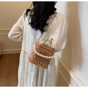 Detail of hand-woven straw bucket bag with pearl handle and gold chain strap