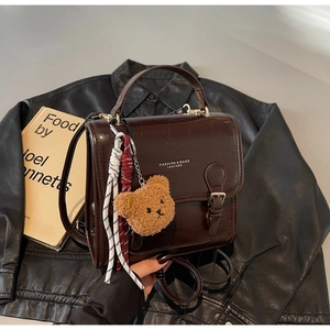 Detail of dark brown retro leather handbag with plush charm and woven rope decoration