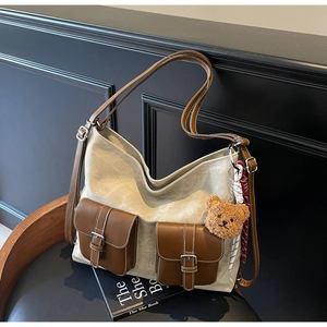Detail of vintage canvas tote bag with leather pockets and cute teddy bear charm on wood chair