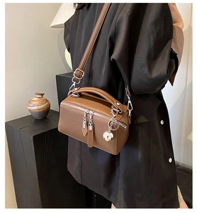 Detail of a brown textured Boston bag with silver hardware and spherical metal charm