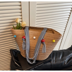 Detail of woven straw tote bag with colorful pom poms and blue striped ribbon handles
