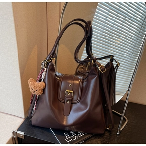Detail of vintage brown leather tote bag with gold buckle and cute bear plush charm