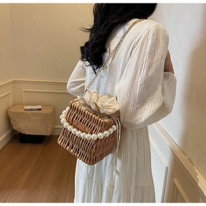 Detail of hand-woven straw bucket bag with pearl handle and golden chain strap
