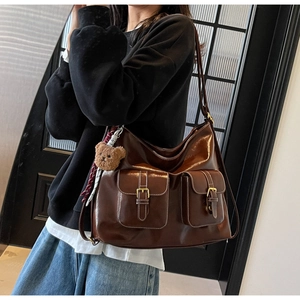 Detail of high-gloss brown PU leather shoulder bag with vintage pockets and bear charm