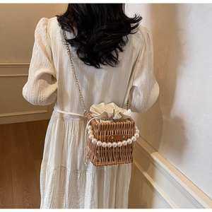 Detail of woven straw bucket bag featuring pearl handle and gold chain strap