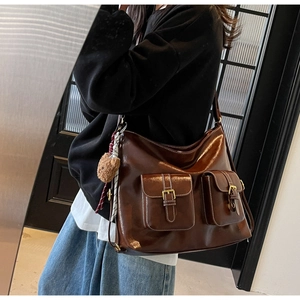 Detail of dark brown glossy leather tote bag with dual front pockets and bear charm