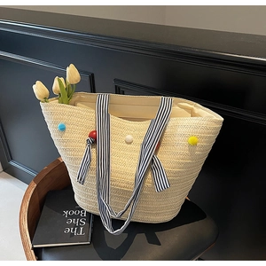 Detail of woven straw tote bag with colorful pom-poms and striped handles in lifestyle setting