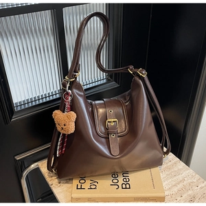 Detail of a dark coffee hobo bag with glossy synthetic leather texture and a plush bear charm