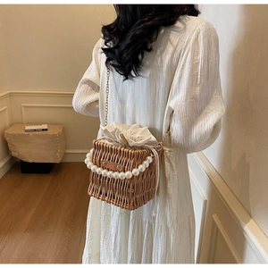 Detail of woven straw bucket bag featuring large pearl handle and gold chain strap