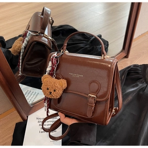 Detail view of brown leather handbag with silk scarf, plush bear charm and gold text