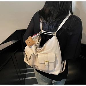 Close-up of cream leather tote bag with functional pockets and a cute bear charm