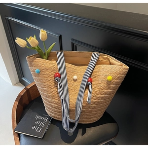 Detail of woven straw tote bag with colorful pom-poms and striped handles on a vintage chair