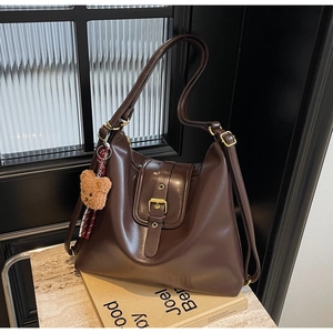 Detail of retro chocolate leather shoulder bag with gold buckle and bear charm