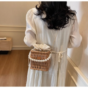 Detail view of woven straw bucket bag with pearl handle and golden chain on a model