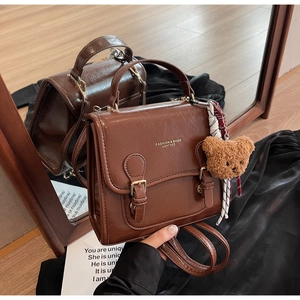 Detail shot of a brown retro PU leather handbag with metallic buckles and a plush bear charm