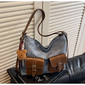 Detail of blue denim crossbody bag featuring brown leather pockets and a plush bear charm