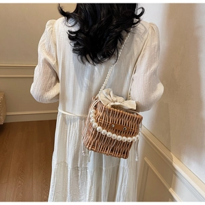 Elegant woman wearing white dress holding straw bucket bag with pearl chain straps