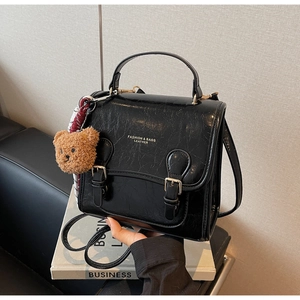 Detail of black glossy PU leather handbag with metal buckles and cute plush bear charm