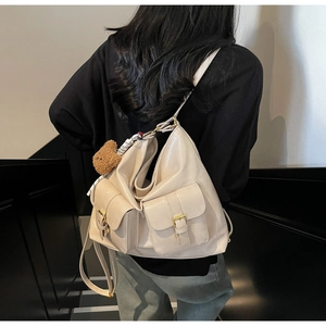 Detail shot of ivory glossy PU tote bag with functional pockets and plush bear charm decoration