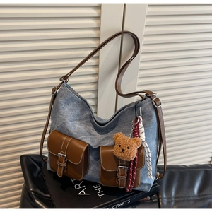 Detail of blue denim tote bag with brown leather pockets and a cute plush bear charm