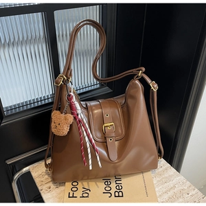 Detail of brown PU leather tote bag with golden buckle, plush bear charm and woven tassel