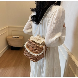 Detail shot of woven straw bucket bag featuring large pearls and elegant pearl chain strap