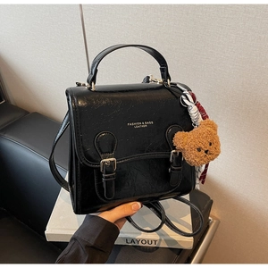 Detail of black faux leather backpack with metallic buckles and a brown plush bear charm