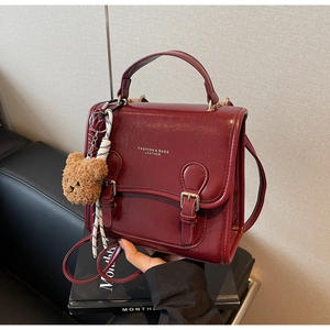 Close-up of deep wine red retro handbag with glossy oil wax leather and teddy bear charm