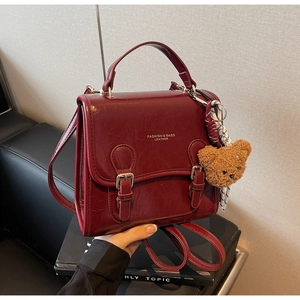 Detail of vintage dark red leather handbag with gold buckles, plush bear and plaid scarf