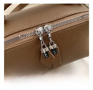 Detail view of brown lychee grain leather handbag with dual metal zippers and leather charms