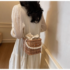 Detail of woven straw bucket bag featuring pearl handle and drawstring lining shown on model