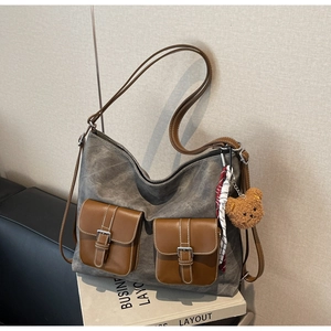 Detail of grey canvas hobo bag featuring brown leather pockets and a plush bear charm