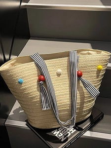 Large straw tote bag with colorful pom-poms and striped handles for summer beach vacations