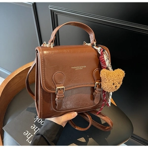 Detailed view of a brown glossy leather backpack with a plush bear charm on a seat
