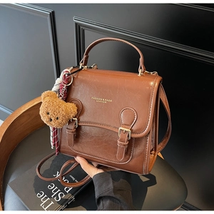 Detail view of brown pebbled leather satchel with gold buckles and plush bear charm