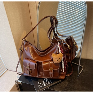Close-up of brown faux leather bag with two buckle pockets and a cute plush bear charm