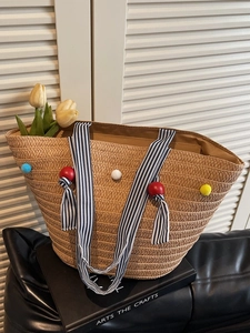 Large woven straw beach bag with colorful pompoms and striped handles for summer vacation