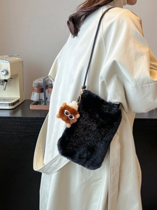 Sac bandoulière en peluche noire avec breloque monstre sur un trench-coat blanc