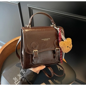 Detail of a dark brown faux leather backpack with gold lettering and a plush bear charm