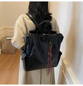 Sac à dos rétro en cuir noir avec pompon porté par un modèle dans un cadre épuré
