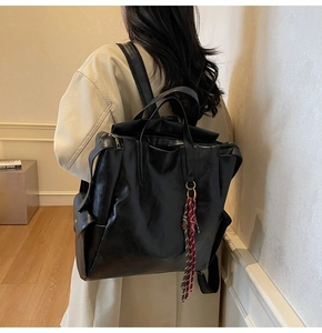 Gros plan d'un grand sac à dos noir en cuir avec double poignée et charme de gland rouge