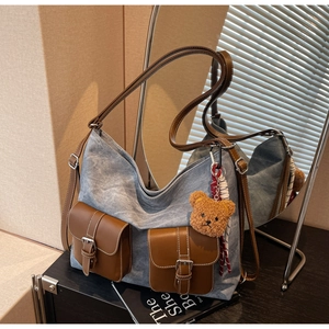 Detail of blue denim tote bag with brown leather pockets and a cute plush bear charm