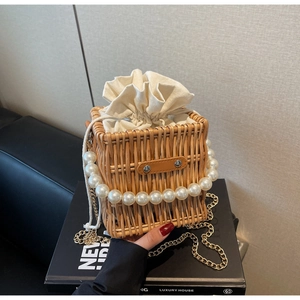 Close-up of woven straw handbag featuring pearl handle and drawstring canvas liner