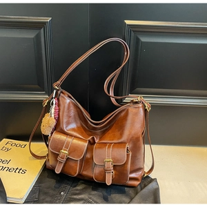 Detail view of brown vintage leather tote with dual buckle pockets and bear charm