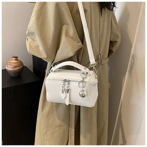 Detail of white Boston bag with litchi texture, silver zipper, and ball charm