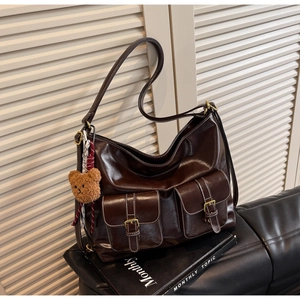 Detail of dark brown tote bag with front pockets, metallic buckles and a bear charm