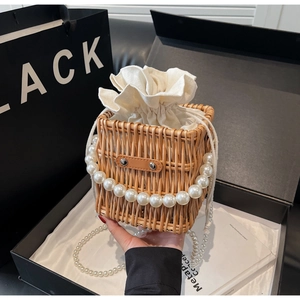 Detail of hand-woven straw bucket bag featuring elegant pearl chain handle in luxury gift box
