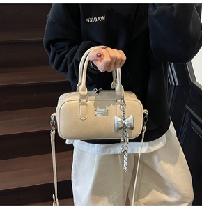 Detalle de bolso Boston blanco crema con placa metálica y colgante de lazo en color plata