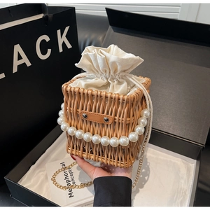 Detail of hand-woven straw bucket bag with large pearl handle and gold chain strap