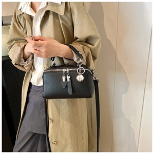 Close-up of black litchi grain leather Boston bag featuring silver zippers and orb pendant